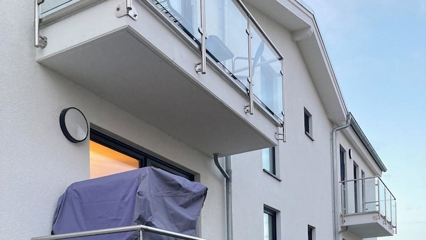 Un edificio moderno con balcón, ventana cubierta y cielo despejado.