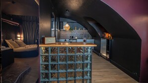 A modern interior with a curved ceiling, a central island with a wooden top, and a kitchen area with a hanging light fixture. - Luxury Love Room (Grasse)