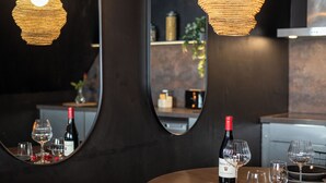 A dining area with a round table, wine glasses, and a bottle of wine. There are two large mirrors on the wall and a hanging light fixture. - Luxury Love Room (Grasse)
