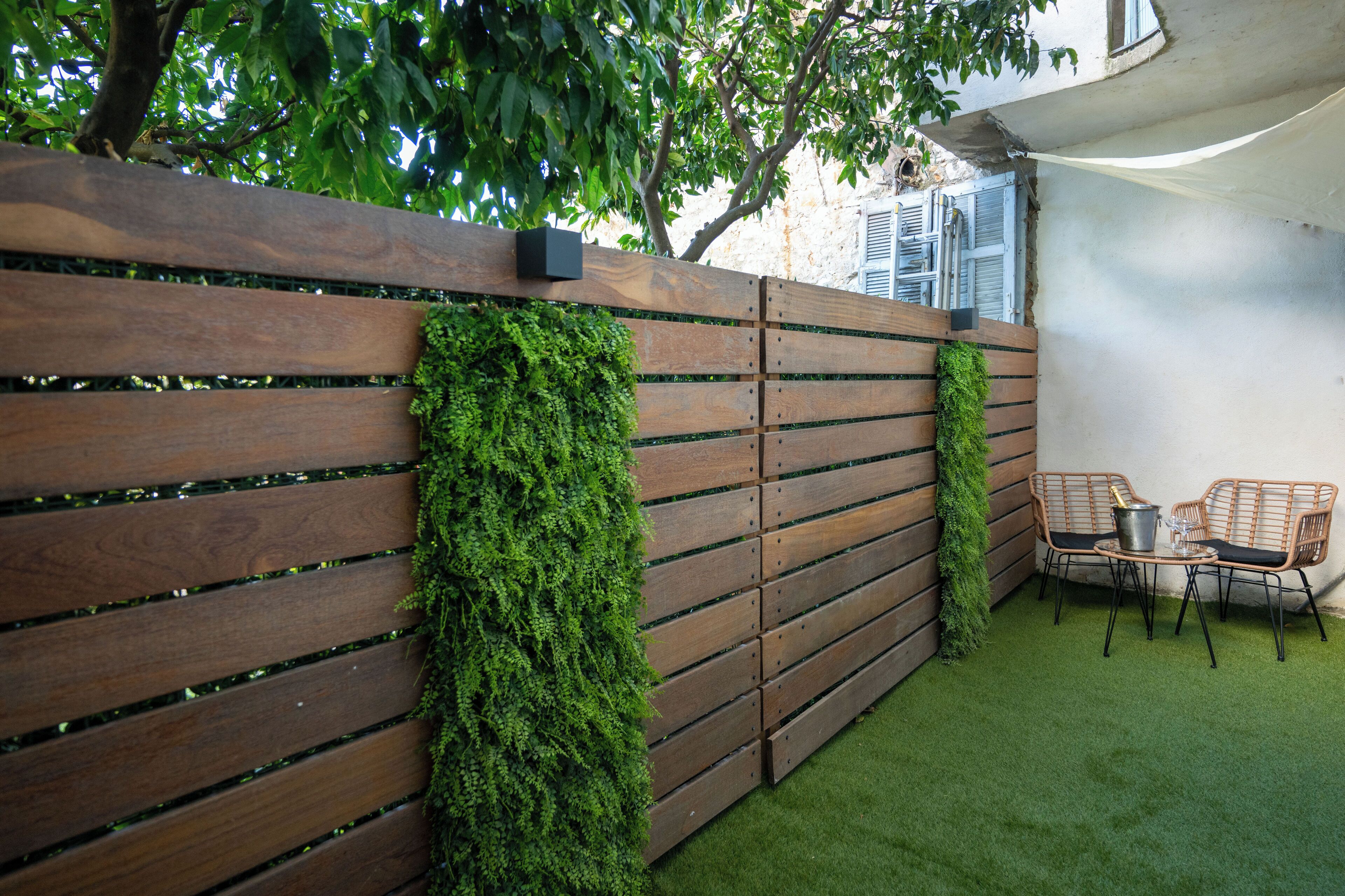 A wooden fence with green foliage, a small table with chairs, and artificial grass.