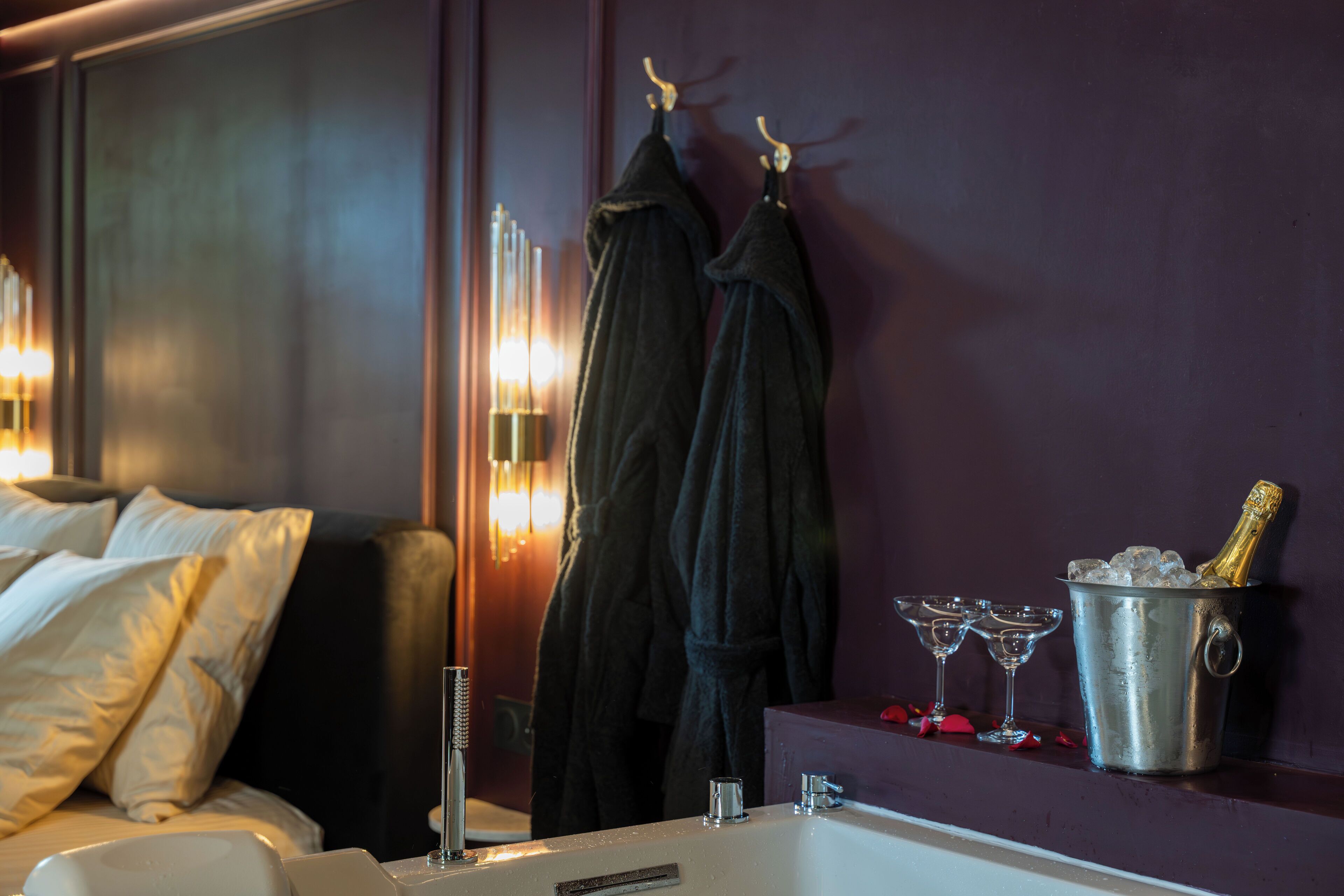 Une chambre d'hôtel comprenant un lit, une baignoire, un porte-peignoir avec des peignoirs, une bouteille de champagne et deux verres.