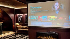 A modern living room with a fireplace, a large screen displaying a movie, and a cozy seating area. - Luxury Love Room (Grasse)
