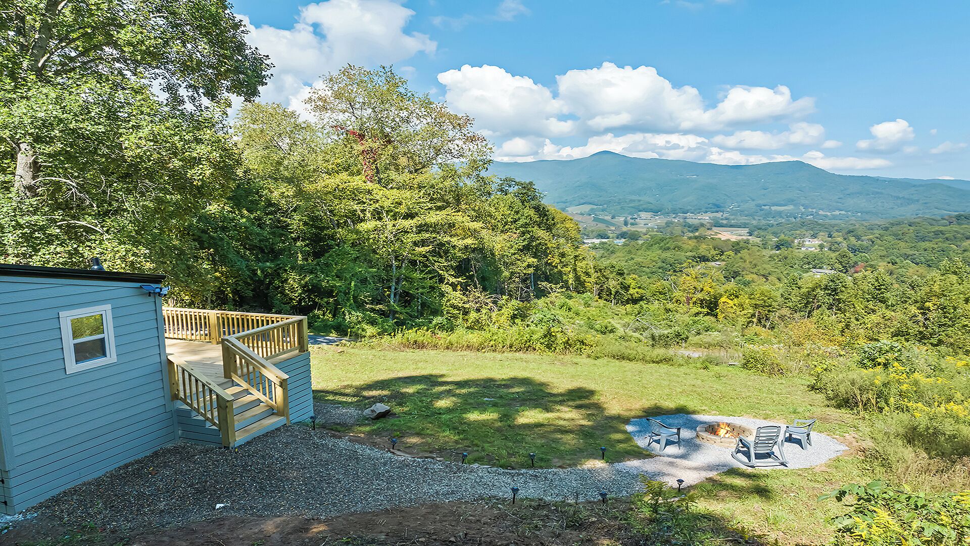 A cabin with a deck, a fire pit, and a view of a mountainous landscape.