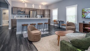 A modern kitchen with a central island, bar stools, and a seating area with a sofa and chairs.