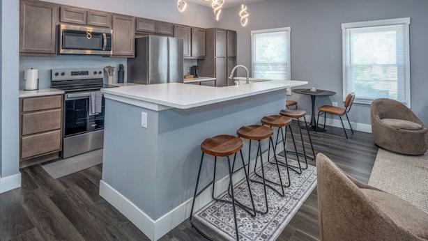 A modern kitchen with a central island, bar stools, and a seating area with a chair.