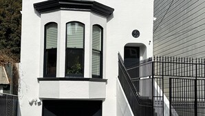 Una casa de dos pisos con una puerta de garaje negra, un pequeño porche delantero y una valla de metal negro.