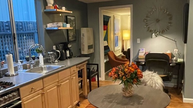 Una cocina moderna con comedor, que incluye una mesa redonda con un jarrón de flores, armarios de madera y vistas de la ciudad a través de grandes ventanales.