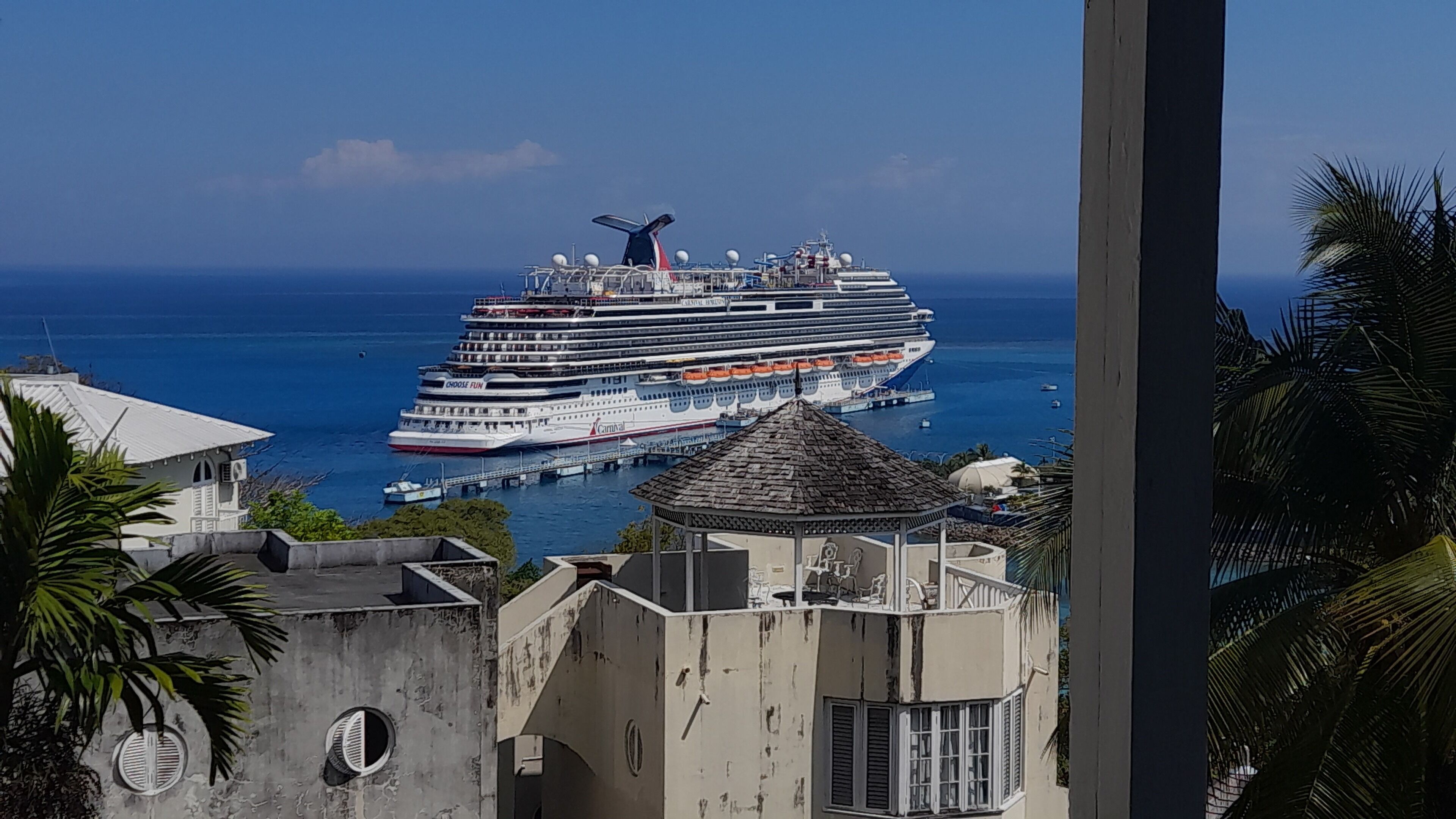 A large cruise ship docked at a port with a view of the ocean and nearby buildings.