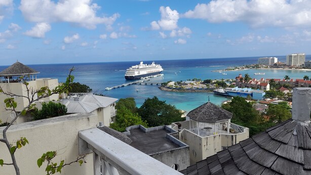 A cruise ship docked at a pier with clear blue waters and a view of a coastal town with buildings and greenery. - Ocho Rios Luxury Ocean View (Ocho Rios)