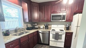 A kitchen with dark wooden cabinets, a stainless steel sink, a microwave, a stove, and a ceiling fan. - Emerald Escape - POOL! (Beckley)