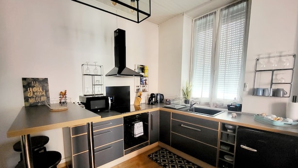 A modern kitchen with a wooden countertop, black cabinets, a black stove, and a window with blinds. - Furnished stopover (Belfort)