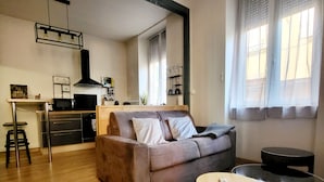 A modern living room with a sofa, a round table, and a kitchen area in the background. - Furnished stopover (Belfort)