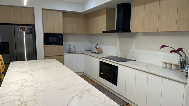 A modern kitchen with white cabinets, a marble countertop, a built-in oven, and a black range hood. - Relaxing Acreage Retreat – Pool, Spa & Media Room (Karalee)