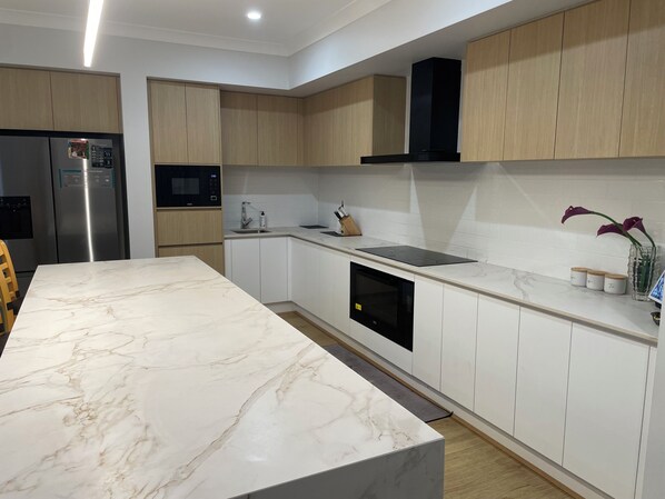 A modern kitchen with white cabinets, a marble countertop, a built-in oven, and a black range hood. - Relaxing Acreage Retreat – Pool, Spa & Media Room (Karalee)