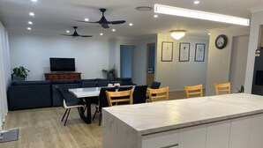 A modern kitchen with a marble countertop, wooden chairs, and a dining table. - Relaxing Acreage Retreat – Pool, Spa & Media Room (Karalee)