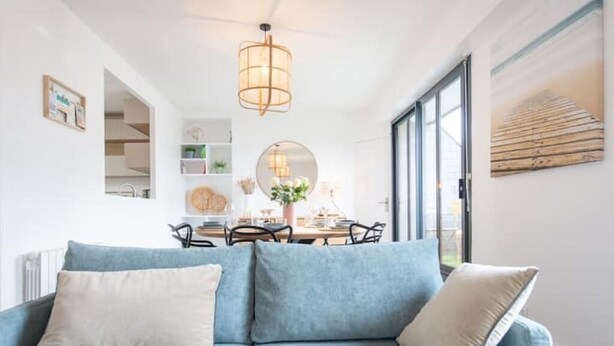 Una sala de estar moderna con un sofá azul, un espejo redondo y un comedor con mesa y sillas.