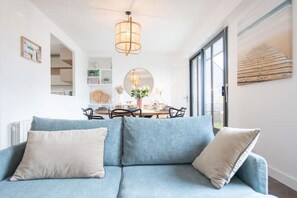Een moderne woonkamer met een blauwe bank, een ronde spiegel en een eethoek met een tafel en stoelen.