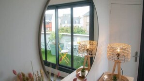 Una habitación con un ventanal grande, una lámpara de mimbre y una mesita con una planta.