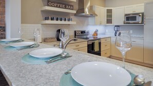 Een moderne keuken met witte kastjes, een ingebouwde magnetron en een bord met daarop 'koffiebar'.