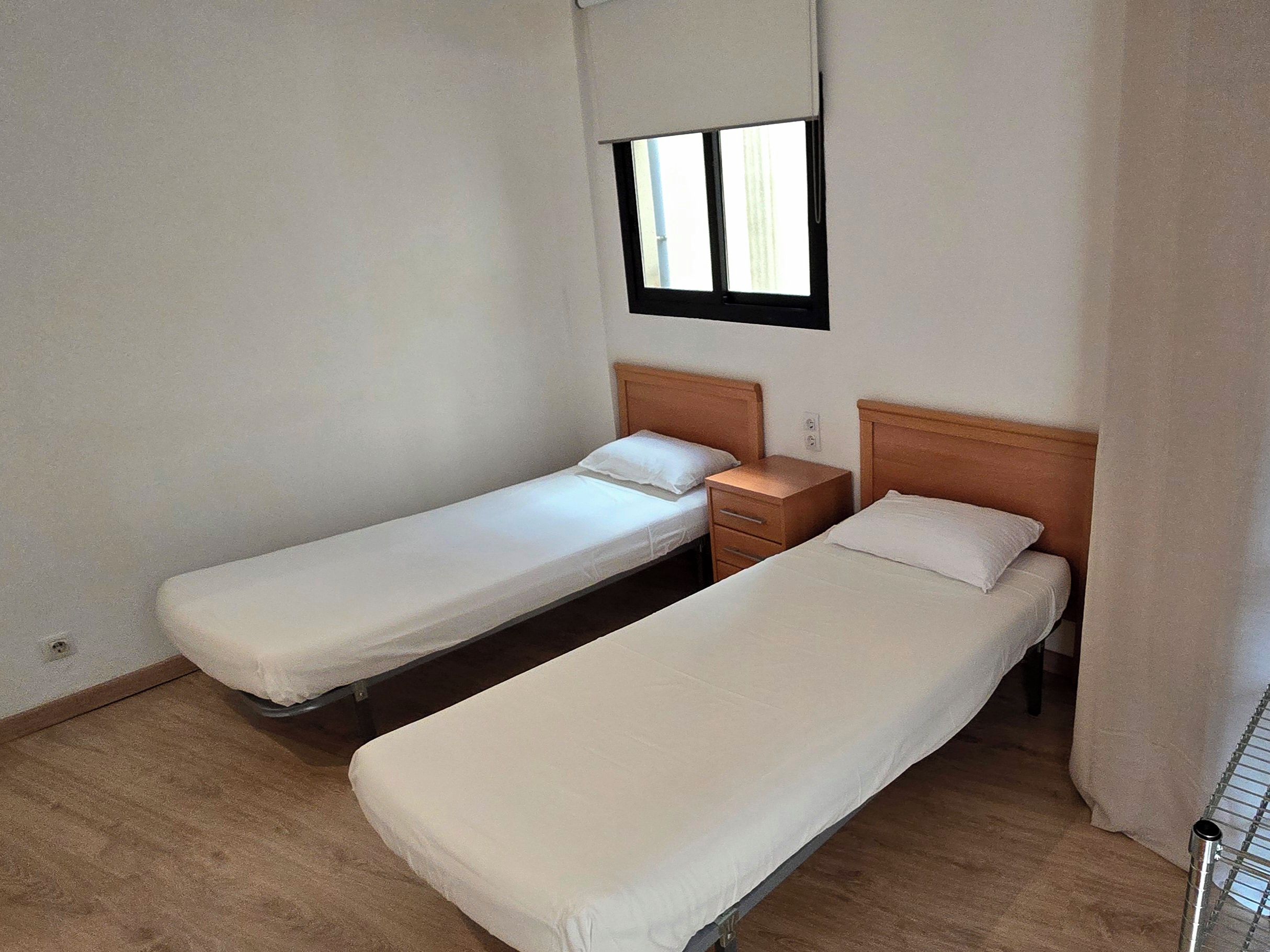 Un alojamiento pequeño, una habitación individual con dos camas individuales, una mesita de noche y una ventana con persianas.