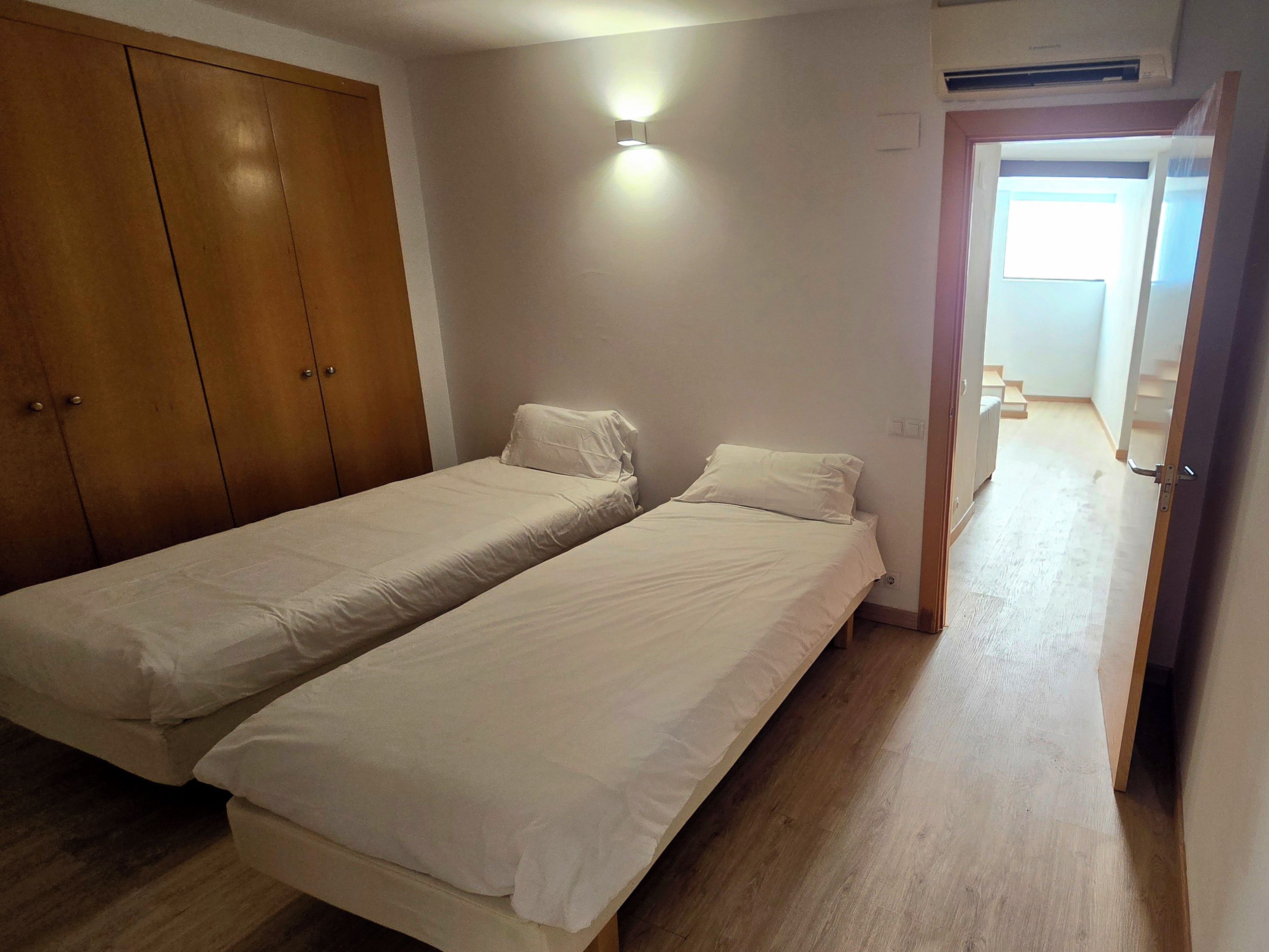 Una habitación con dos camas individuales, un armario, una lámpara y una puerta que da a otra habitación.