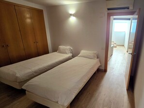 A room with two single beds, a wardrobe, a light fixture, and a door leading to another room.