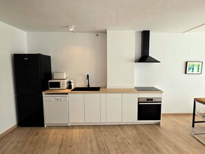 Una cuina compacta amb un frigorífic negre, armaris blancs, un microones, una torradora, un rentatelles i una campana extractora negra.