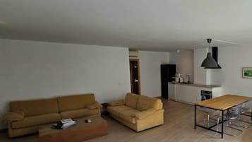 Sala de estar con sofá, mesa de centro y mesa de comedor con sillas. Hay una zona de cocina con refrigerador, microondas y lavamanos.