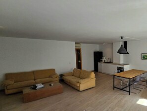 Sala de estar con sofá, mesa de centro y mesa de comedor con sillas. Hay una zona de cocina con refrigerador, microondas y lavamanos.
