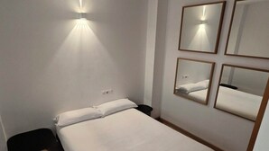 A hotel room with a bed, a wall-mounted mirror, and a light fixture.