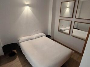 Habitación de hotel con cama, espejo montado en la pared y lámpara.