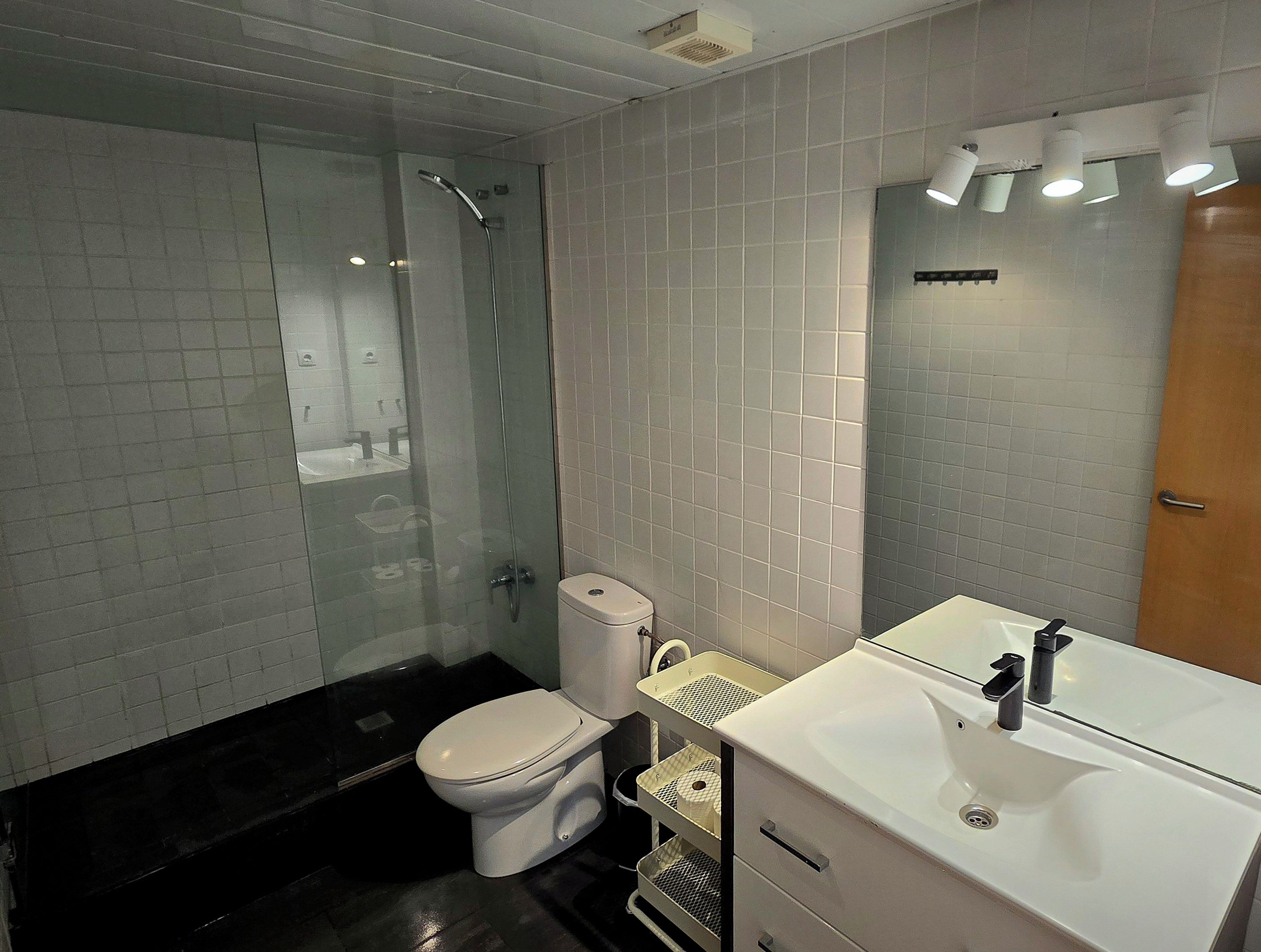 Un baño moderno con ducha envuelta en vidrio, inodoro y lavamanos con espejo superior.