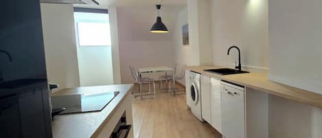 A compact kitchen with a washing machine, a sink, and a dining area with chairs.