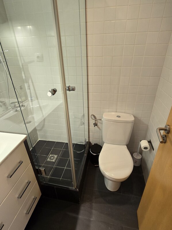 Un baño con ducha envuelta en vidrio, inodoro y lavabo con gabinete.