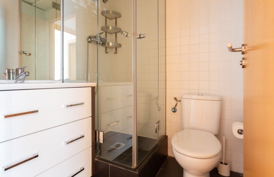 Un baño moderno con cabina de ducha de vidrio, inodoro blanco y tocador con cajones.