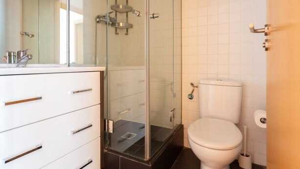 A modern bathroom with a glass shower enclosure, a white toilet, and a vanity with drawers.