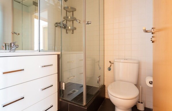Un baño moderno con cabina de ducha de vidrio, inodoro blanco y tocador con cajones.