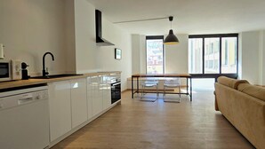 A modern kitchen with white cabinets, a Bosch dishwasher, and a black faucet. There is a dining area with a table and chairs, and a sofa in the living room.