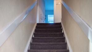 Een tapijtsvloer met witte trapleuning, die leidt naar een kamer met een blauwe muur en een witte deur.