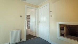 Een hal met een radiator, een witte deur en een raam met uitzicht op een kamer.