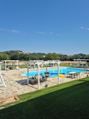 A pool area with lounge chairs and a pergola, surrounded by a grassy lawn and a view of distant hills. - Agriturismo Case Corboli Villetta Rufino (Todi)