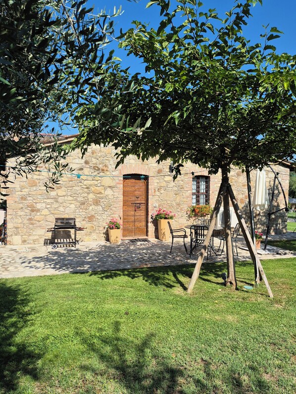 A stone building with a wooden door, outdoor seating, and potted plants. - Agriturismo Case Corboli Villetta Rufino (Todi)
