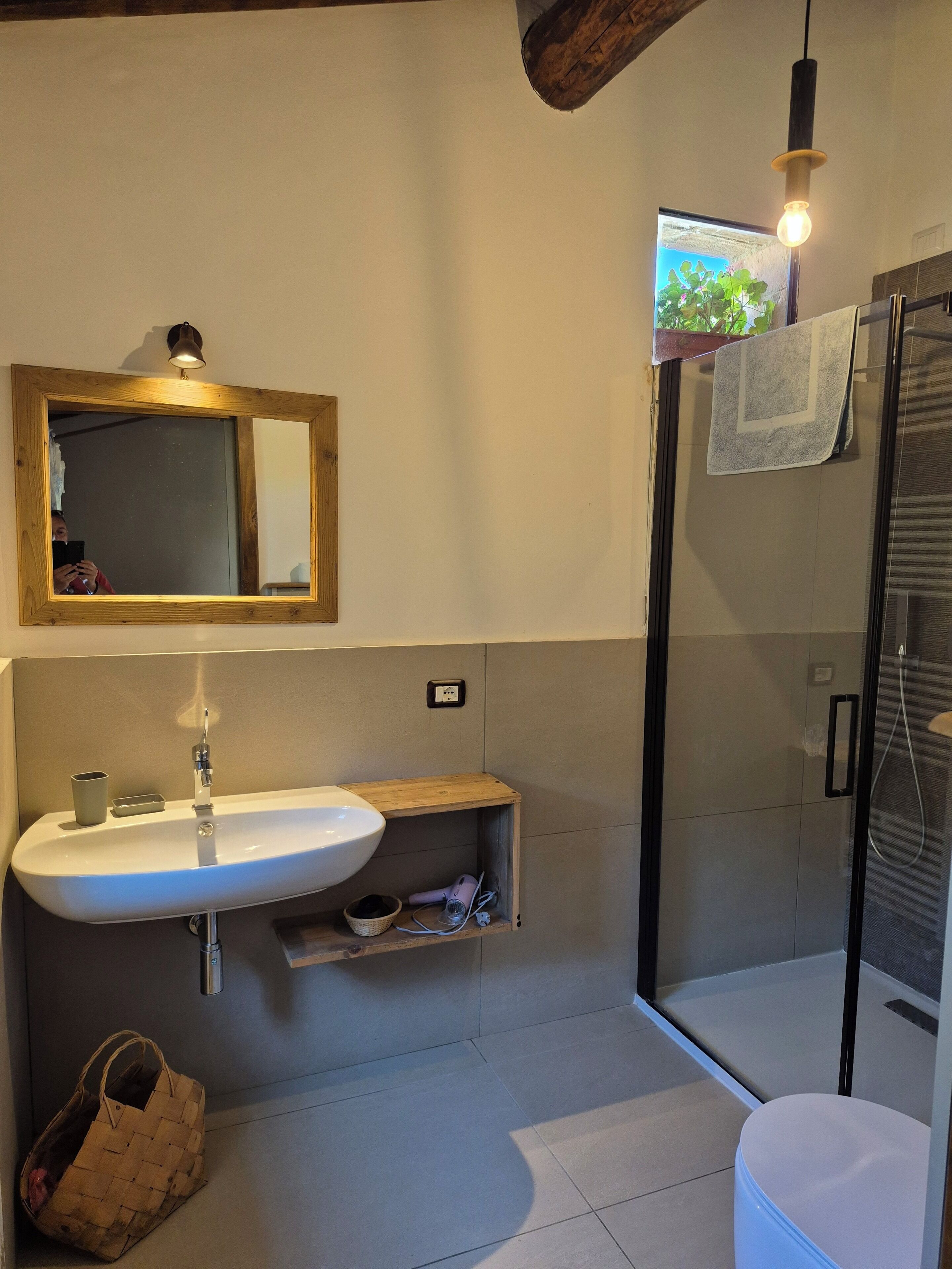 Een badkamer met een houten wastafelmeubel, een grote spiegel, een wastafel, een handdoekrek en een douchecabine met glazen wanden.