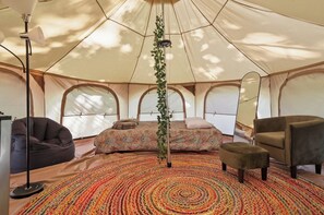 A tent with a bed, a chair, a bean bag, and a lamp.