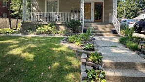 Una casa de dos plantas con un porche delantero, un pequeño jardín frontal con borde de piedra y un garaje.