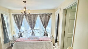 Un dormitorio con cama, una silla, una mesita y una lámpara.