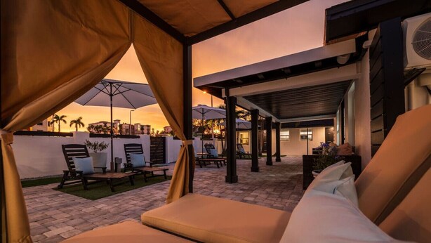 Un espace extérieur aménagé avec des fauteuils confortables et des parasols, une terrasse couverte et une vue sur le coucher du soleil.