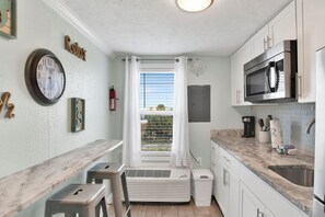 A compact kitchen with a built-in microwave, a stainless steel sink, and a window with curtains. - Steps to Beach & The Hangout • Walk Everywhere • Covered Parking (Orange Beach)