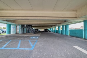 Ein überdachter Parkbereich mit einem blauen Parkplatz für Behinderte, einer Treppe zu einem Ausgang und einer Reihe geparkter Autos.