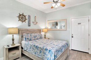 A bedroom with a bed, nightstands, a ceiling fan, a door, and wall decorations including a ship's wheel and an anchor. - Steps to Beach & The Hangout • Walk Everywhere • Covered Parking (Orange Beach)